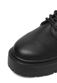 Czarne skórzane buty z zaokrąglonym noskiem i teksturowaną powierzchnią. Posiadają grubą, czarną gumową podeszwę z bieżnikiem zapewniającym przyczepność. W zestawie sznurowadła.