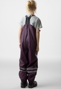 Purple waterproof overalls with gray reflective stripes, adjustable shoulder straps, and elasticated cuffs. Worn over a gray shirt.