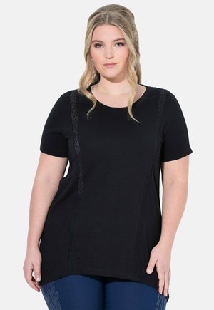 Zwarte t-shirt met korte mouwen en kantdetails langs de zijkanten, voorzien van een ronde halslijn en een ontspannen pasvorm, gecombineerd met blauwe broek.