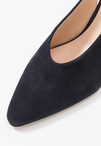 Tmavě modrá semišová lodička na vysokém podpatku s špičatou špičkou a prořezávaným designem, představující hladou vnitřní podšívku a matnou texturu.