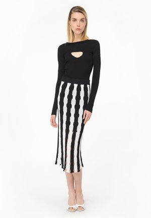 Maglietta nera a maniche lunghe con motivo a costine e un'apertura sul colletto, abbinata a una gonna a righe lunghezza ginocchio con motivi alternati in bianco e nero.