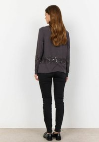 Grijze langemouwen top met sequinaccenten aan de zoom, gecombineerd met zwarte slim-fit broek en zwarte schoenen, gezien van achteren.