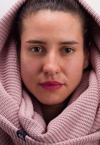 Woven scarf in soft, light pink, featuring a ribbed texture. A silver septum ring adds detail to the face framed by the scarf.