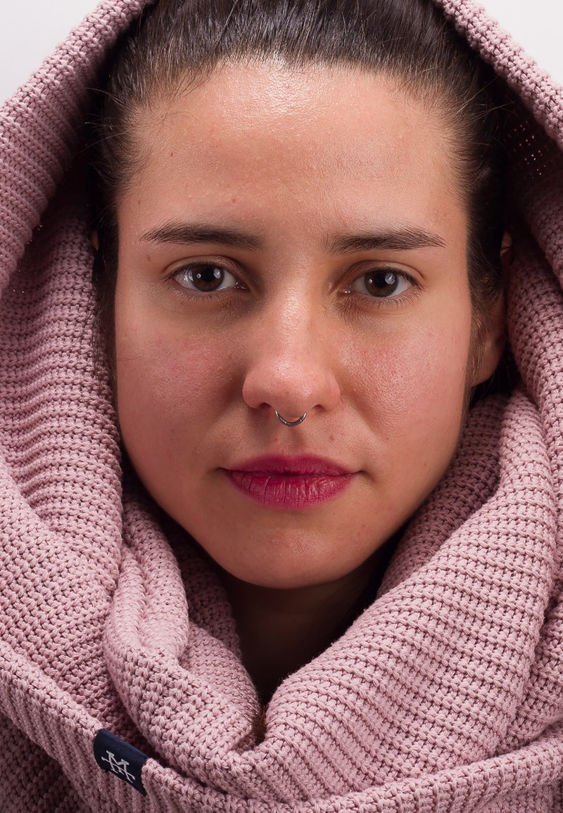 Woven scarf in soft, light pink, featuring a ribbed texture. A silver septum ring adds detail to the face framed by the scarf.
