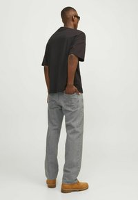 Must musta tee-shirt, lahti lõige; heledat hallid teksad; pruuni töösaapad; sile tekstuur; juhuslik disain; seisev poos.