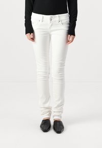 Hvite skinny jeans med fem lommer, beltehemper og knappelukking, kombinert med svarte firkantede flate sko. Jevnt, elastisk stoff.