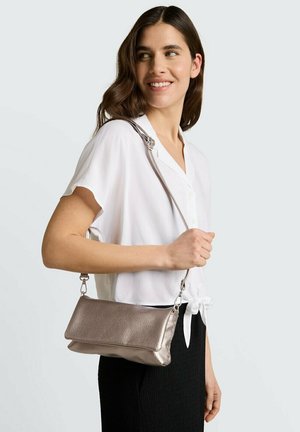 Woman wearing white short-sleeve blouse and black skirt, holding a metallic silver shoulder bag, smiling and looking to the side.