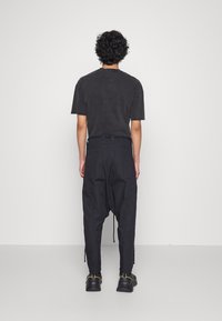 Schwarzes Baumwoll-T-Shirt mit kurzen Ärmeln, kombiniert mit einer lockeren schwarzen Hose mit elastischen Bündchen und seitlichen Reißverschlüssen. Einfarbig, schlichtes Design.