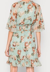 Blumenkleid aus leicht grünem, transparentem Stoff mit Rüschensäumen und -saum. Es verfügt über rosa und orangefarbene Blumen mit goldenen, vertikalen Akzenten.