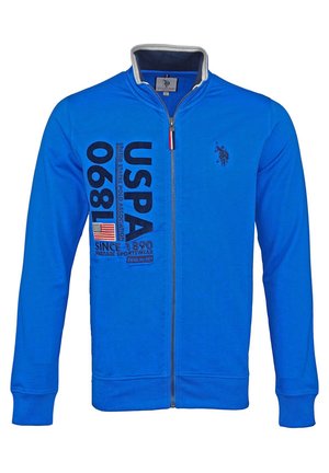 Niebieska bluza rozpinana z tekstem USPA 1890, naszywką amerykańskiej flagi i małym logo gracza polo na piersi, z wysokim kołnierzem.