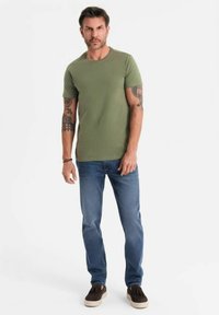 Olivově zelené tričko s krátkým rukávem vyrobené z bavlny, doplněné modrými džíny. Model má na sobě hnědé slip-on boty. Jednoduchý design, bez vzorů.