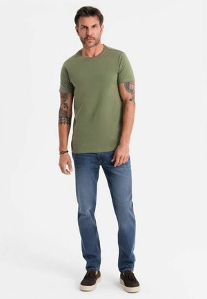 Olivově zelené tričko s krátkým rukávem vyrobené z bavlny, doplněné modrými džíny. Model má na sobě hnědé slip-on boty. Jednoduchý design, bez vzorů.