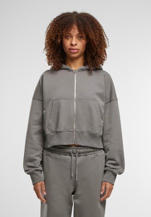 Gekürzte graue Zip-Hoodie aus weichem Stoff, mit Kapuze, Fronttaschen und weiten Ärmeln. Kombiniert mit passenden Jogginghosen.