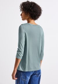 Top azzurro chiaro a maniche lunghe con scollatura rotonda e maniche a tre quarti, realizzato in materiale morbido, abbinato a jeans di denim blu.