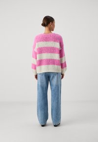 Maglione di grandi dimensioni a maglia con righe rosa e bianche, finitura testurizzata, scollatura rotonda e maniche ampie, abbinato a jeans leggermente azzurri a gamba larga.