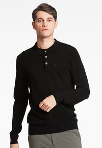 Sort langærmet polo skjorte med krave, tre knapper og ribbede mansjetter. Har et diskret logo på brystet og en glat tekstur.