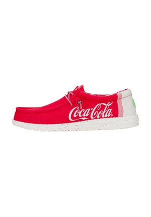 Red fabric slip-on shoes featuring a white sole, accented with a Coca-Cola logo and splatter pattern. Rounded toe and simple lace detailing.