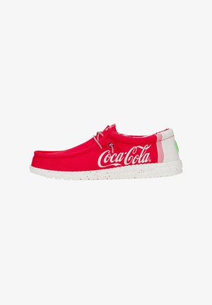 Scarpe slip-on in tessuto rosso con suola bianca, decorate con il logo della Coca-Cola e un motivo a schizzi. Punta rotonda e semplice dettaglio in pizzo.