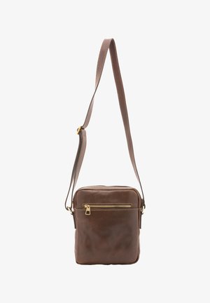 Bruine leren crossbodytas met verstelbare riem en voorvak met rits, hangend tegen een witte achtergrond.