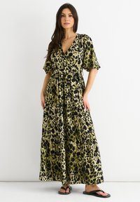 Maxi dress with a wrap design, featuring a green and black animal print, short puff sleeves, and a belted waistline. Light, flowing fabric.