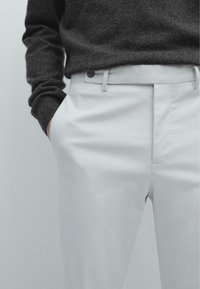 Białe, dopasowane spodnie z bawełny o gładkiej fakturze, z zapięciem na guzik i kieszeniami bocznymi, w połączeniu z ciemnoszarym swetrem.