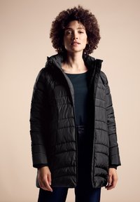 Abrigo negro tipo puffer con patrón acolchado y capucha, que contrasta con una parte superior oscura debajo. Cuenta con una cremallera frontal y bolsillos laterales.