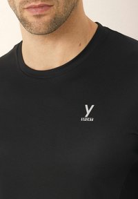 Černé sportovní tričko s ribbovanou strukturou, kulatým výstřihem a malým stříbrným logem s nápisem "Y SPORT" na levé straně.