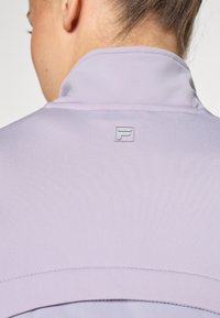 Svijetlopurple sportska jakna s visokim ovratnikom. Glatka tekstura, s malim srebrnim logotipom na stražnjoj strani. Jednostavan dizajn s suptilnim šavovima.