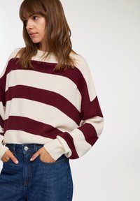 Sweter w paski w kolorze kremowym i burgundowym, z luźnym krojem, szerokimi rękawami i ściągaczami. W zestawie z dżinsami z wysokim stanem.