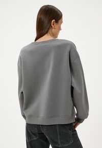 Szary polarowy sweter z luźnym krojem, ribbowanymi mankietami i okrągłym dekoltem, charakteryzujący się gładką strukturą i minimalistycznym wyglądem.