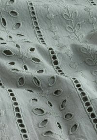 Lys grøn broderet stof med blomster mønstre, udskæringer og tekstureret syning, der skaber et delikat og indviklet design.