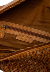 Interno di una borsa in pelle intrecciata marrone con tasca con zip e etichetta con la scritta "RE:DESIGNED EST. 2003" cucita all'interno della fodera.