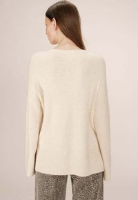 Maglione lavorato a maglia color crema con orlo a coste, spalle cadute e texture morbida, abbinato a pantaloni grigi con motivo. Vista posteriore.