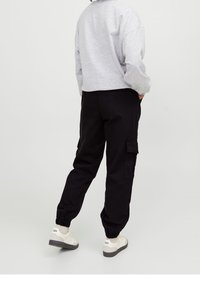 Grå kortärmad sweatshirt, svarta cargobyxor med elastiska mudd, sidofickor och vita sneakers med gråa sulor. Enkel, avslappnad design.