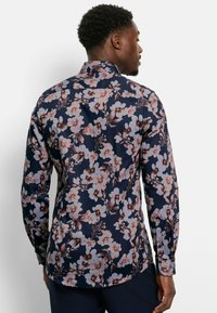 Blumenhemd mit navy Hintergrund und pinken sowie weißen Blumen. Lange Ärmel, kragenförmiges Design und stilvolle Knopfdetails.