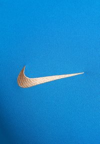 Tessuto sportivo blu con texture a coste, caratterizzato da un prominente logo Nike ricamato in oro sul lato sinistro.