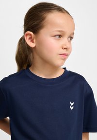 T-shirt à manches courtes bleu marine en tissu lisse, présentant un graphique en chevron blanc sur la poitrine gauche et un col rond.