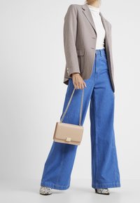 Blazer a scacchi marrone, dolcevita bianco, jeans a vita alta blu a gamba larga, borsa beige con tracolla dorata e scarpe grigie a fantasia.