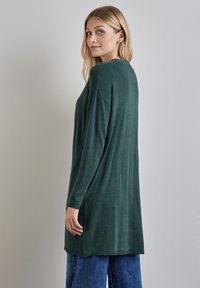 Långärmad, oversized tröja i mörkgrön stickad tyg. Har en rundad halsringning och en lös passform som sträcker sig ner under höfterna.