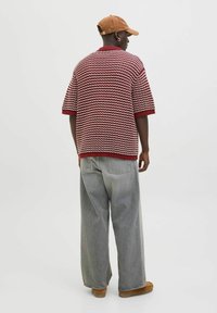 Chemise tricotée à manches courtes, rouge et blanche, avec un col côtelé, associée à un pantalon en denim gris ample et des chaussures marron.