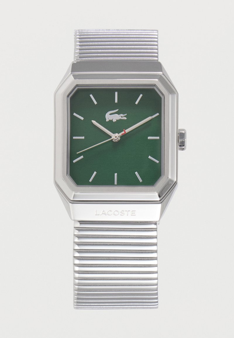Ασημένιο μεταλλικό ρολόι με πράσινο τετράγωνο καντράν, ασημένιους δείκτες ώρας, λογότυπο Lacoste και μεταλλικό λουράκι με πτυχώσεις. Η ώρα δείχνει 10:11:38.