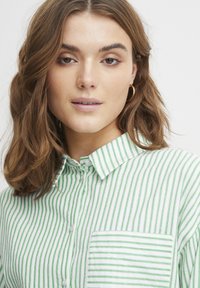Camicia con colletto a righe verticali verdi e bianche, dotata di taschino sul petto e placket con bottoni, realizzata in un morbido tessuto testurizzato.