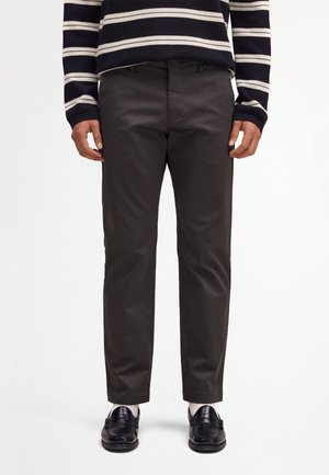 Mężczyzna ubrany w czarne spodnie o prostych nogawkach, czarne mokasyny, białe skarpety oraz czarno-biały sweter w paski z długim rękawem.