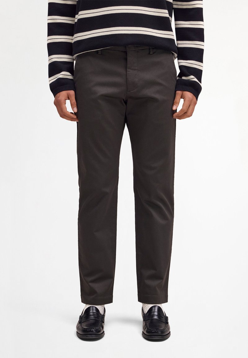 Homme portant un pantalon noir à jambes droites, des mocassins noirs, des chaussettes blanches et un pull à manches longues rayé noir et blanc.