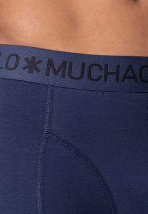 Navy blue boxer briefs featuring a black elastic waistband with "MUCHACHO" text and visible stitching details on a smooth fabric surface.