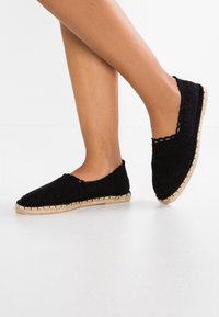 Espadrillas nere intrecciate con suola in juta, caratterizzate da una punta arrotondata e un bordo scallop. Design semplice e leggero, adatto per un abbigliamento casual.