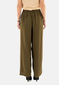 Pantaloni a gamba larga, verde oliva, realizzati in tessuto testurizzato con una vita elastica. Indossati con tacchi neri, visti da dietro.