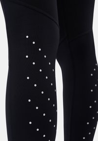 Black athletic leggings with small reflective white dots arranged on the lower thigh and knee area for visibility.