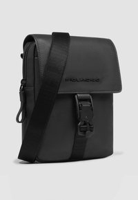 Schwarze Leder-Umhängetasche mit klappbarem Überschlag, verstellbarem Riemen und Schnallenverschluss; verfügt über ein eingeprägtes Markenlogo auf der Vorderseite.