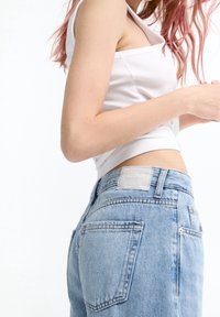 Vaqueros de tela vaquera azul claro con cintura alta y ajuste holgado. Presentan un parche de cuero con la etiqueta "PULL&BEAR" y bolsillos traseros.